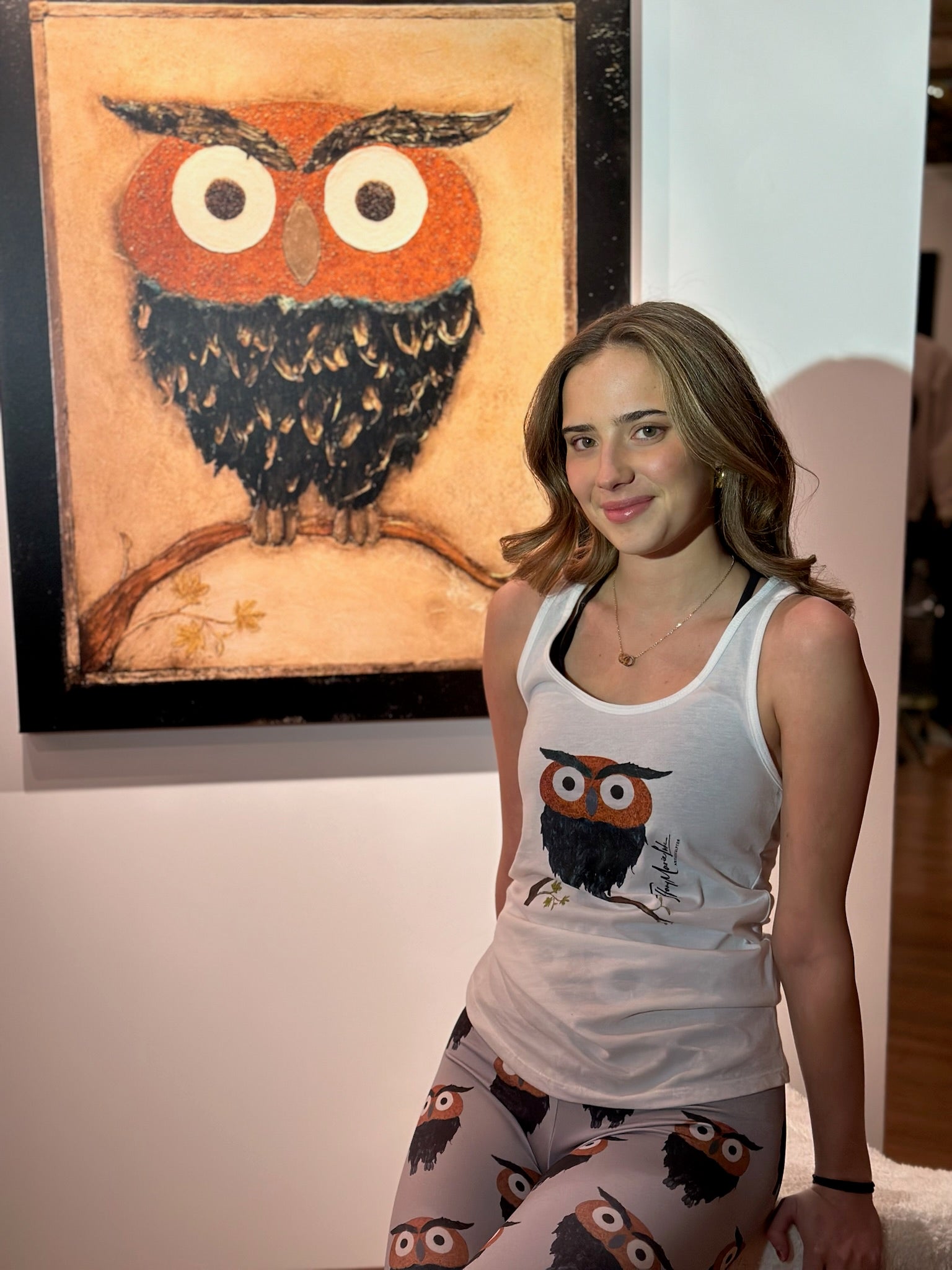 Woman wearing a tank top and leggings with owl design in front of an owl painting.